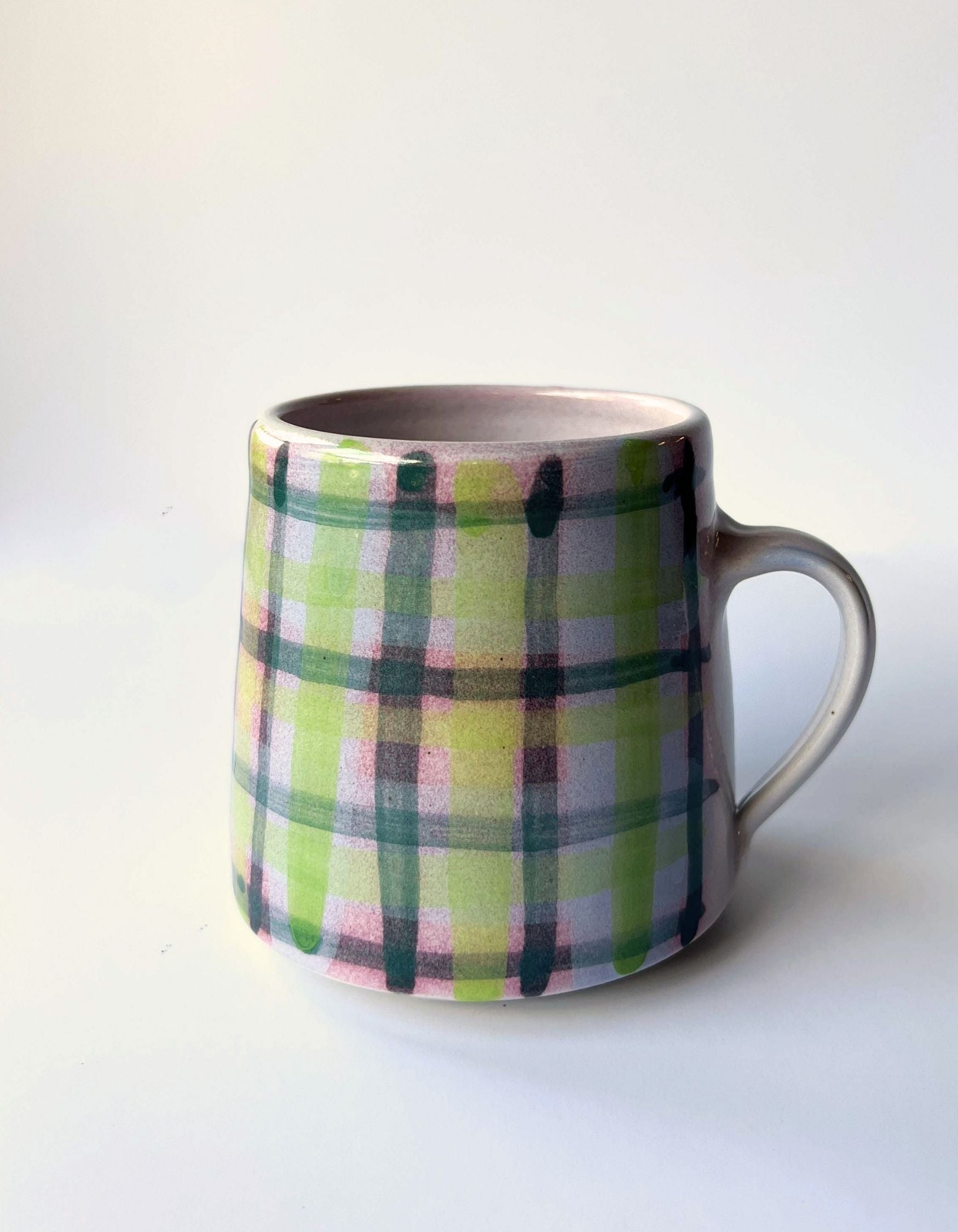 A ceramic mug with a pastel plaid pattern featuring green, pink, and yellow stripes on a white background, with a glossy finish.